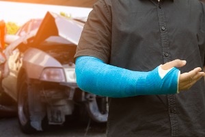 A man with a broken arm standing in front of a totaled car, needing an Auto Accident Lawyer in Pekin IL